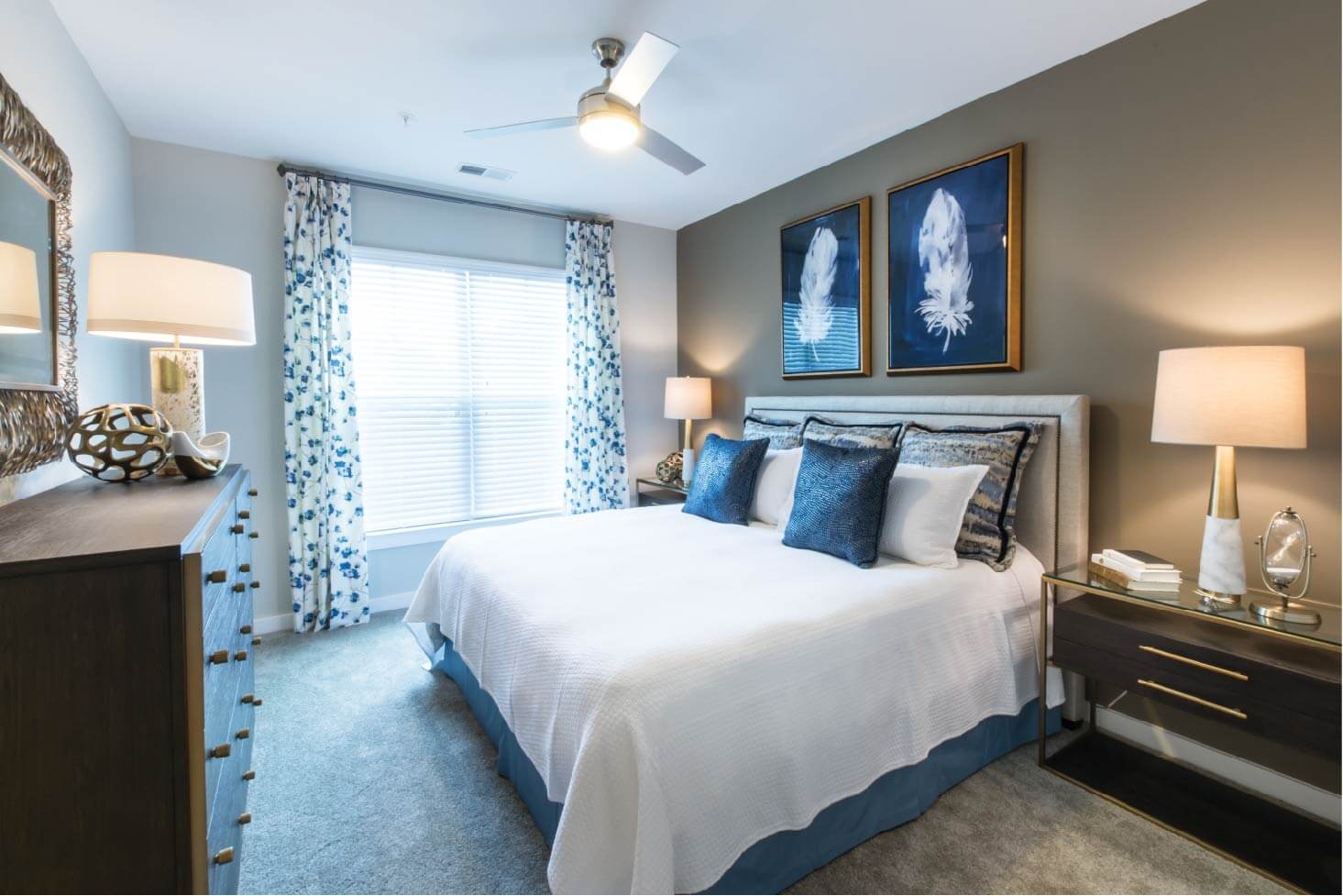 Three Bedroom Apartments in Cary, NC - The Aster - Fully Furnished Bedroom With Carpet, A Large Window, Lighted Ceiling Fan, and Stylish Decor